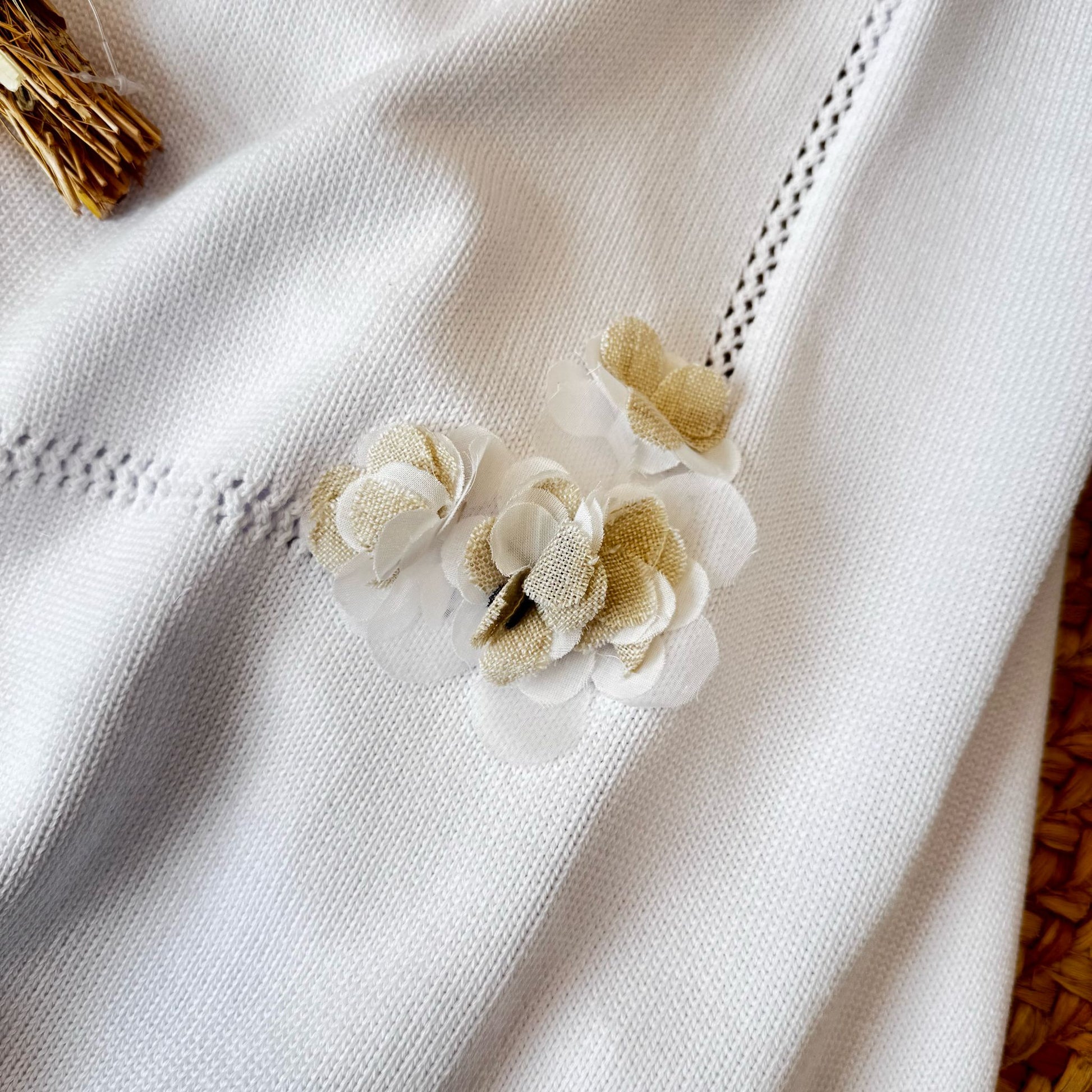 Dettaglio della copertina in maglia con applicazioni floreali per neonato
