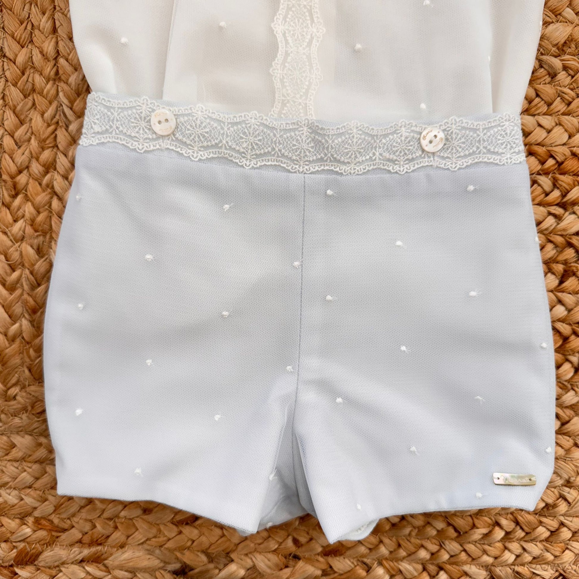 Dettaglio pantaloncino celeste polvere con fascia in pizzo e bottoncini chiari