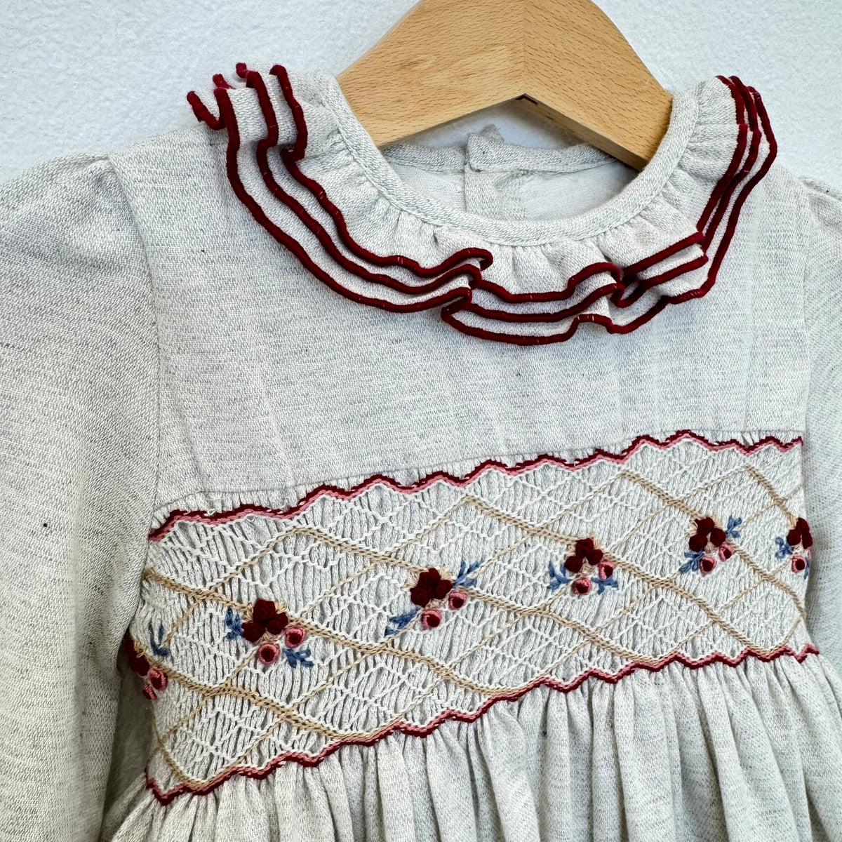 Abito bimba grigio chiaro in cotone con punto smock, ricami floreali e colletto a volant bordeaux.