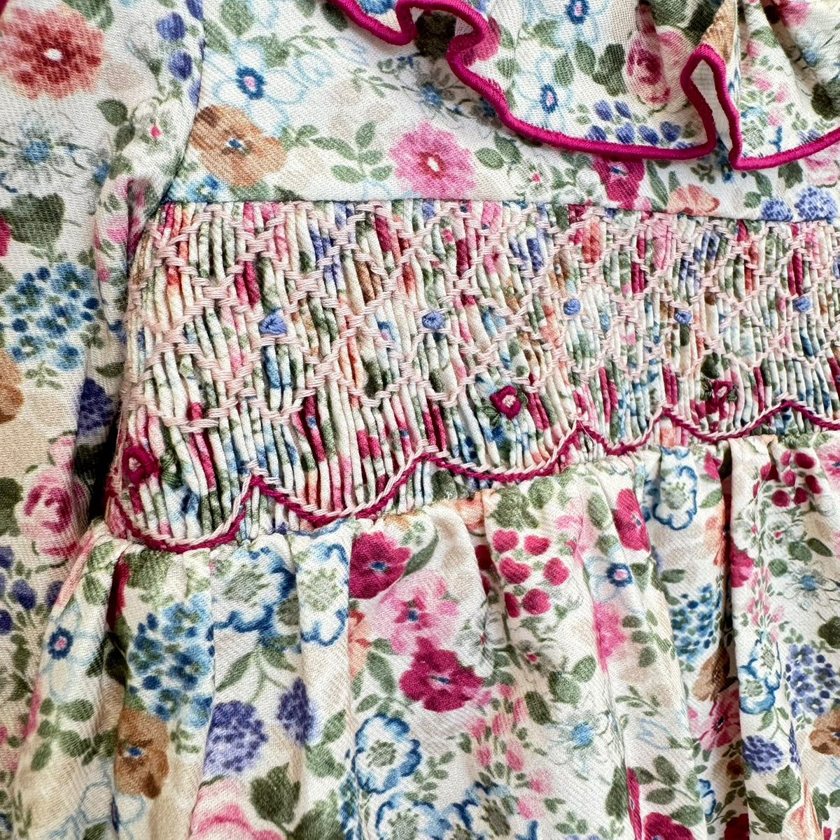 Pagliaccetto bimba floreale in cotone con punto smock e colletto a volant fucsia.
