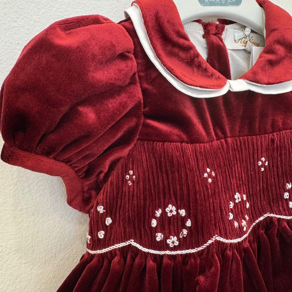 Abito bimba in velluto bordeaux con punto smock, colletto bianco a contrasto e maniche a palloncino.