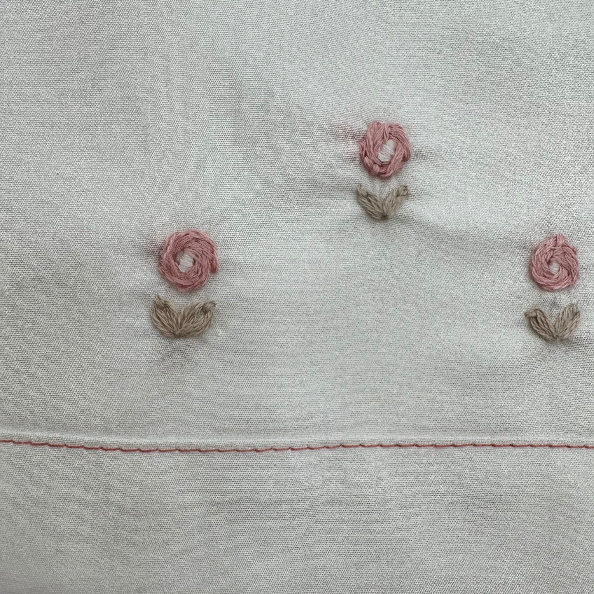 Dettaglio ricamo floreale su lenzuolo culla prima nascita