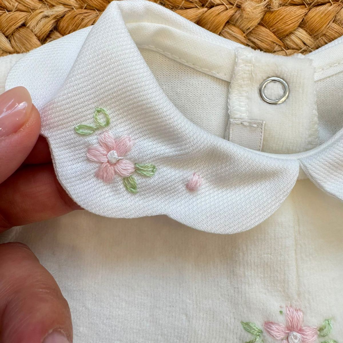Tutina in ciniglia neonata colore latte con colletto ricamato a fiori rosa e ricamo floreale sul davanti.