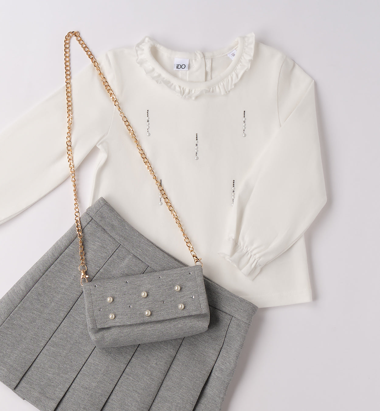 dettaglio maglia bianca con strass, gonna grigia e borsetta con catena dorata