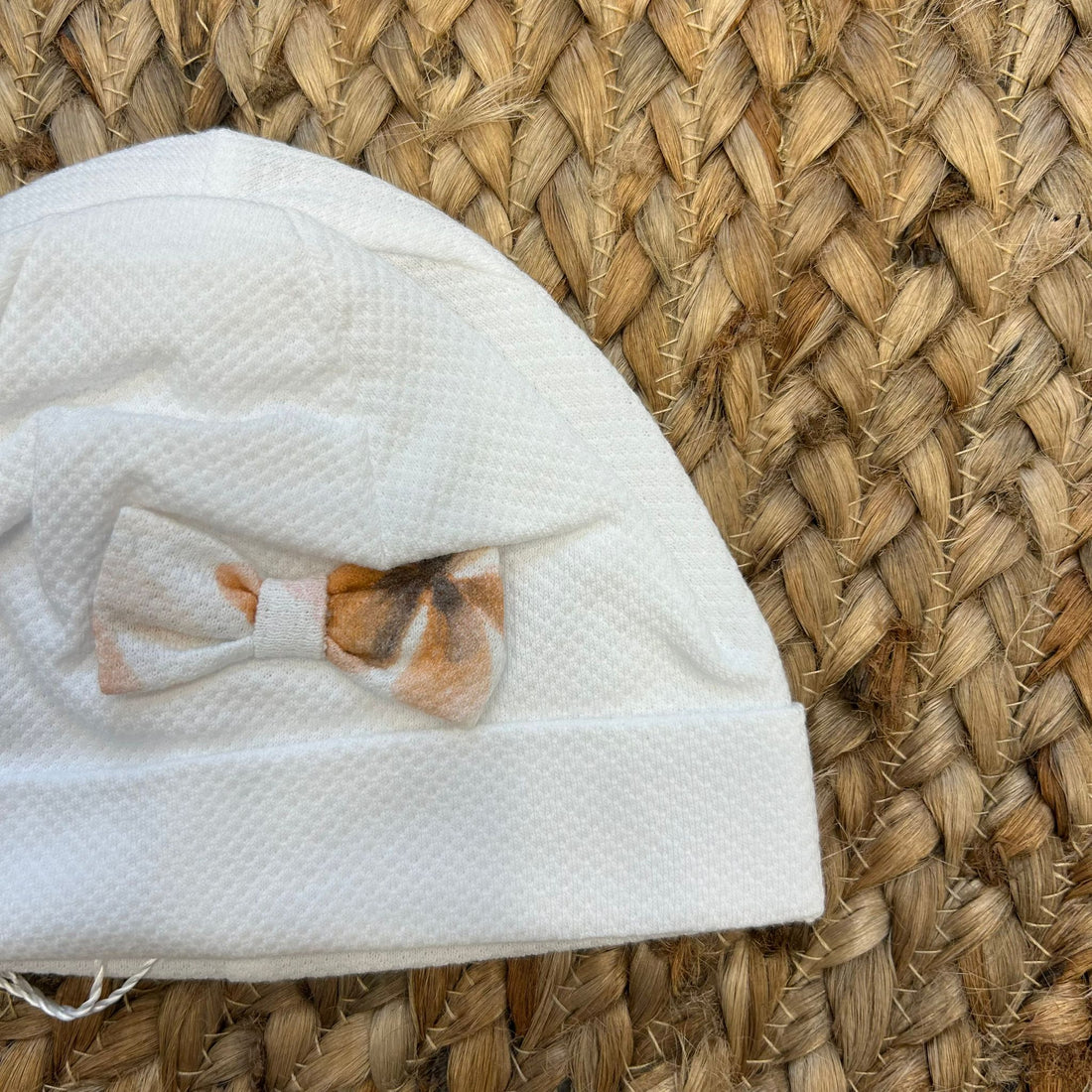 Cuffia neonata bianca con fiocco floreale nei toni pesca e beige.

