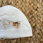 Cuffia neonata bianca con fiocco floreale nei toni pesca e beige.


