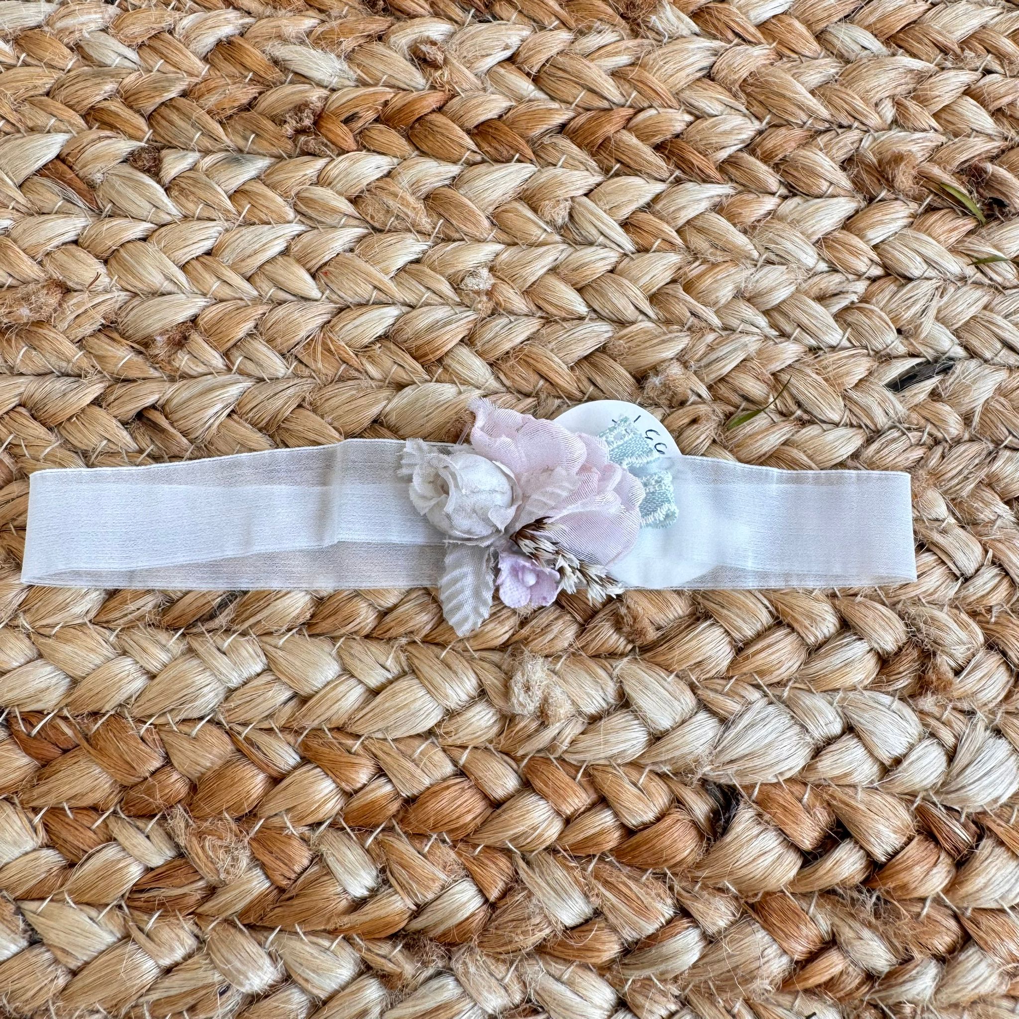 Fascia neonata per battesimo con fiori rosa cipria e spighe naturali su sfondo intrecciato