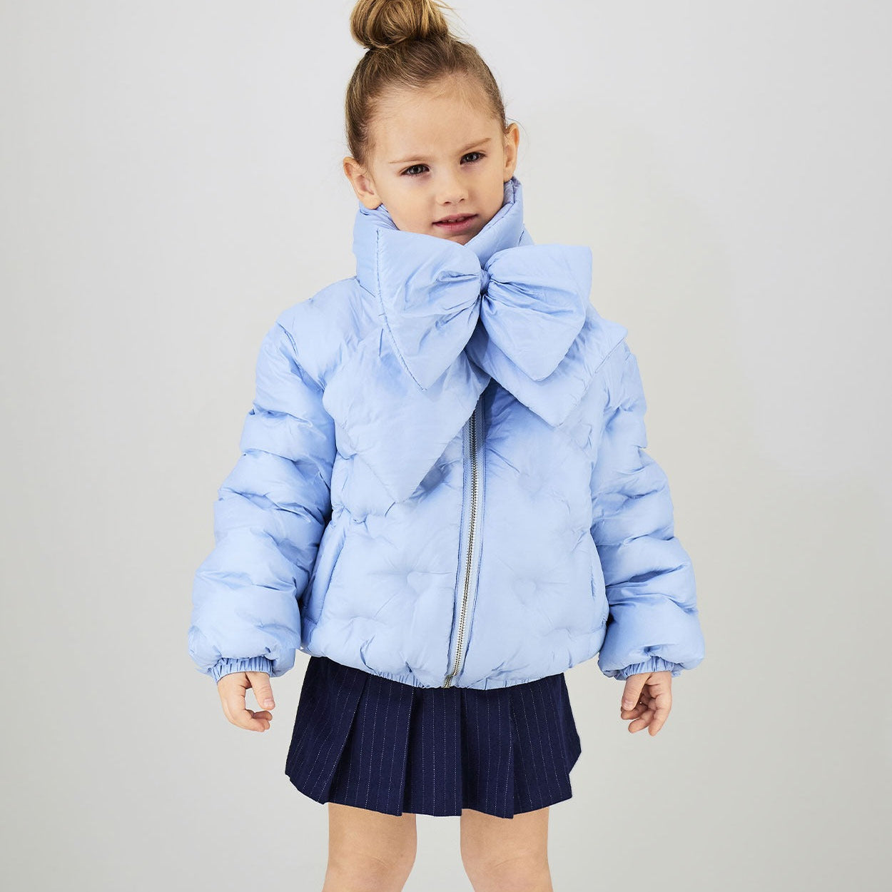 Bambina con giubbotto celeste imbottito e sciarpa coordinata con maxi fiocco
