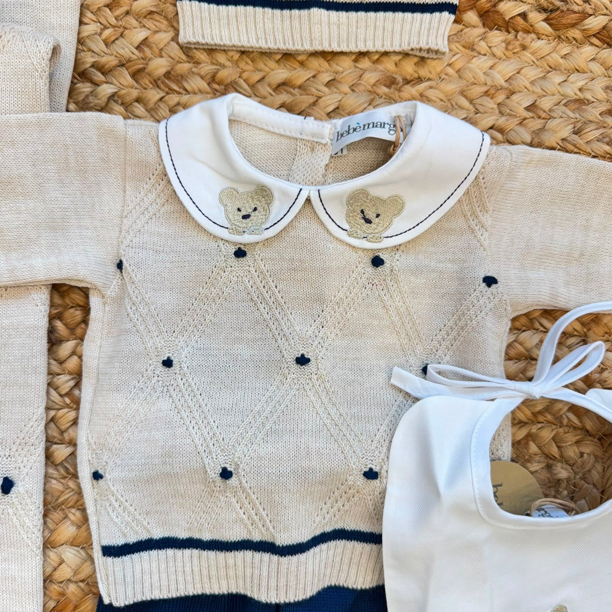 Dettaglio corredino nascita neonato con tessile bianco e orsetto ricamato beige