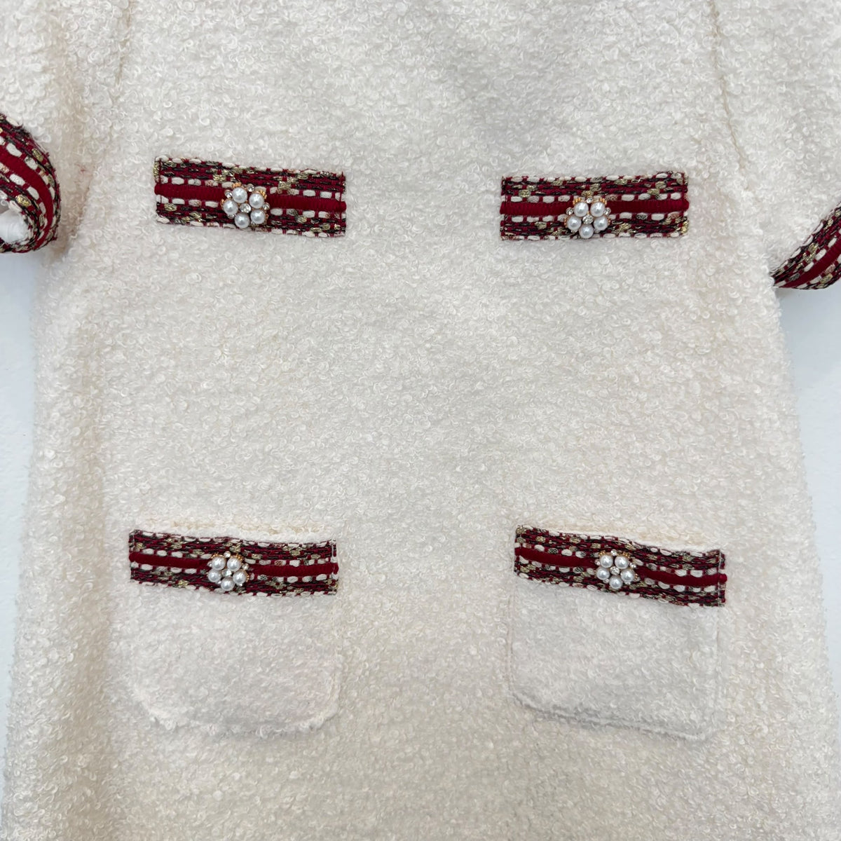Dettaglio abito elegante bambina panna bouclé con passamaneria bordeaux e decorazioni di perline