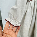 Abito bimba grigio chiaro in cotone con punto smock, ricami floreali e colletto a volant bordeaux.