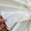 Mantellina da battesimo per neonata color avorio, modello svasato con fiocco frontale e fondo arrotondato.