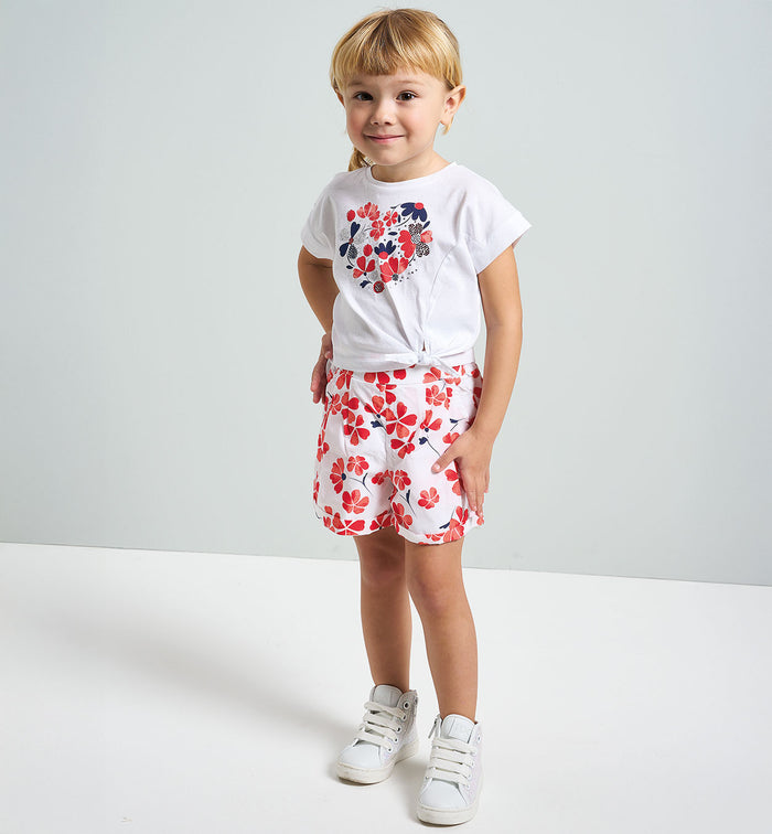 Outfit estivo bambina, t-shirt bianca con cuore floreale e pantaloncini rossi e blu, ideale per cerimonie non troppo formali.