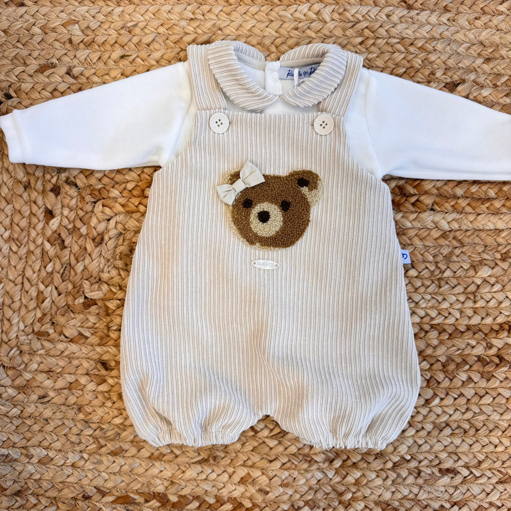 Dettaglio fiocco ricamato sul pagliaccetto in velluto beige per neonata.