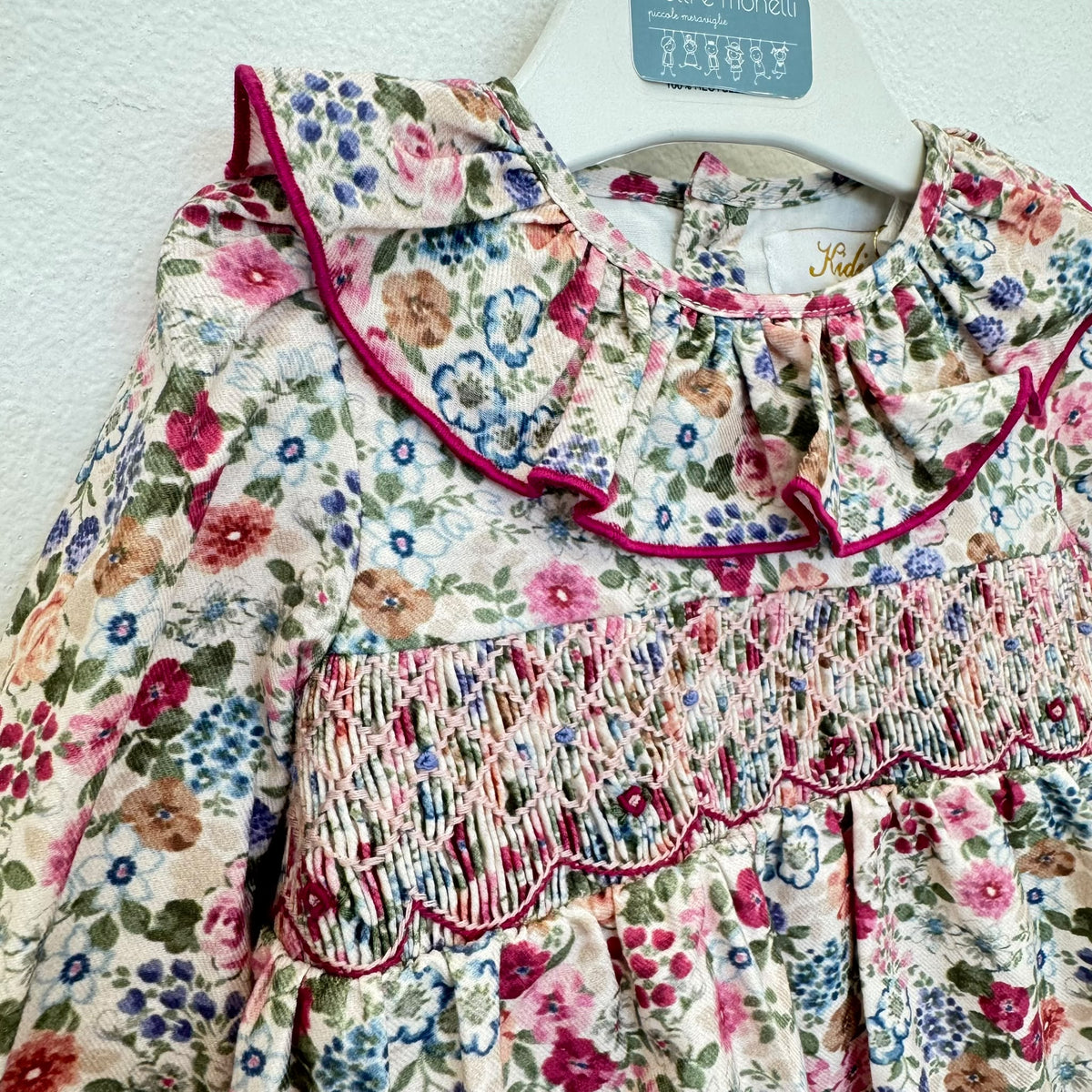 Pagliaccetto bimba floreale in cotone con punto smock e colletto a volant fucsia.