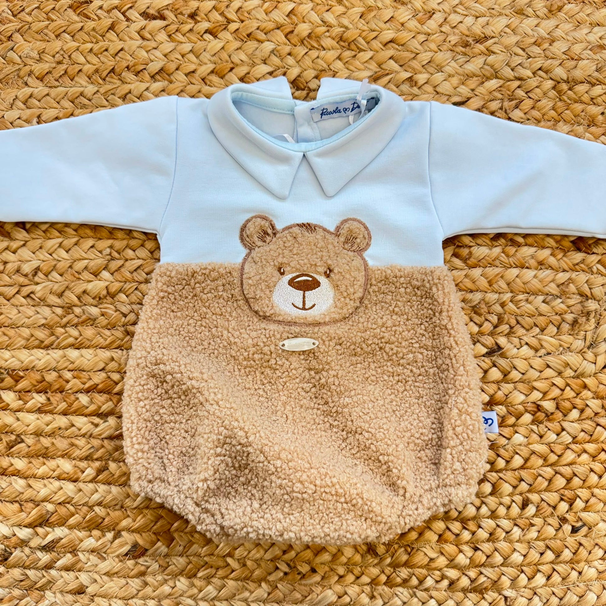 Dettaglio del tessuto teddy e dei bottoni del pagliaccetto neonato azzurro in caldo cotone.