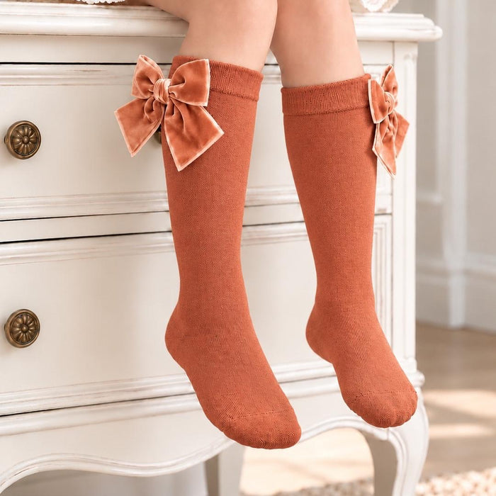 Calzettoni al ginocchio bambina color terracotta chiaro con bordo a costine e grandi fiocchi in velluto.