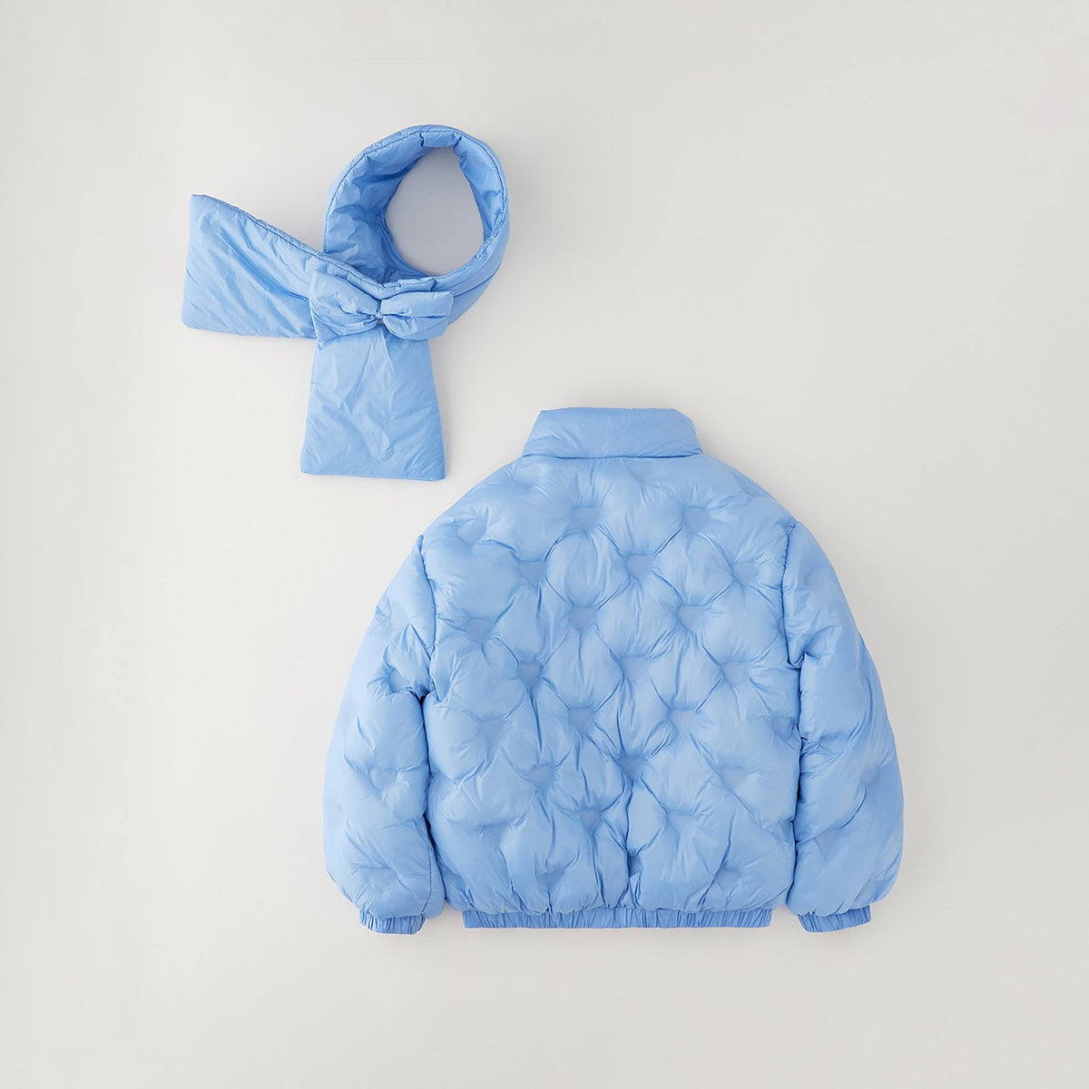 Bambina con giubbotto celeste imbottito e sciarpa coordinata con maxi fiocco