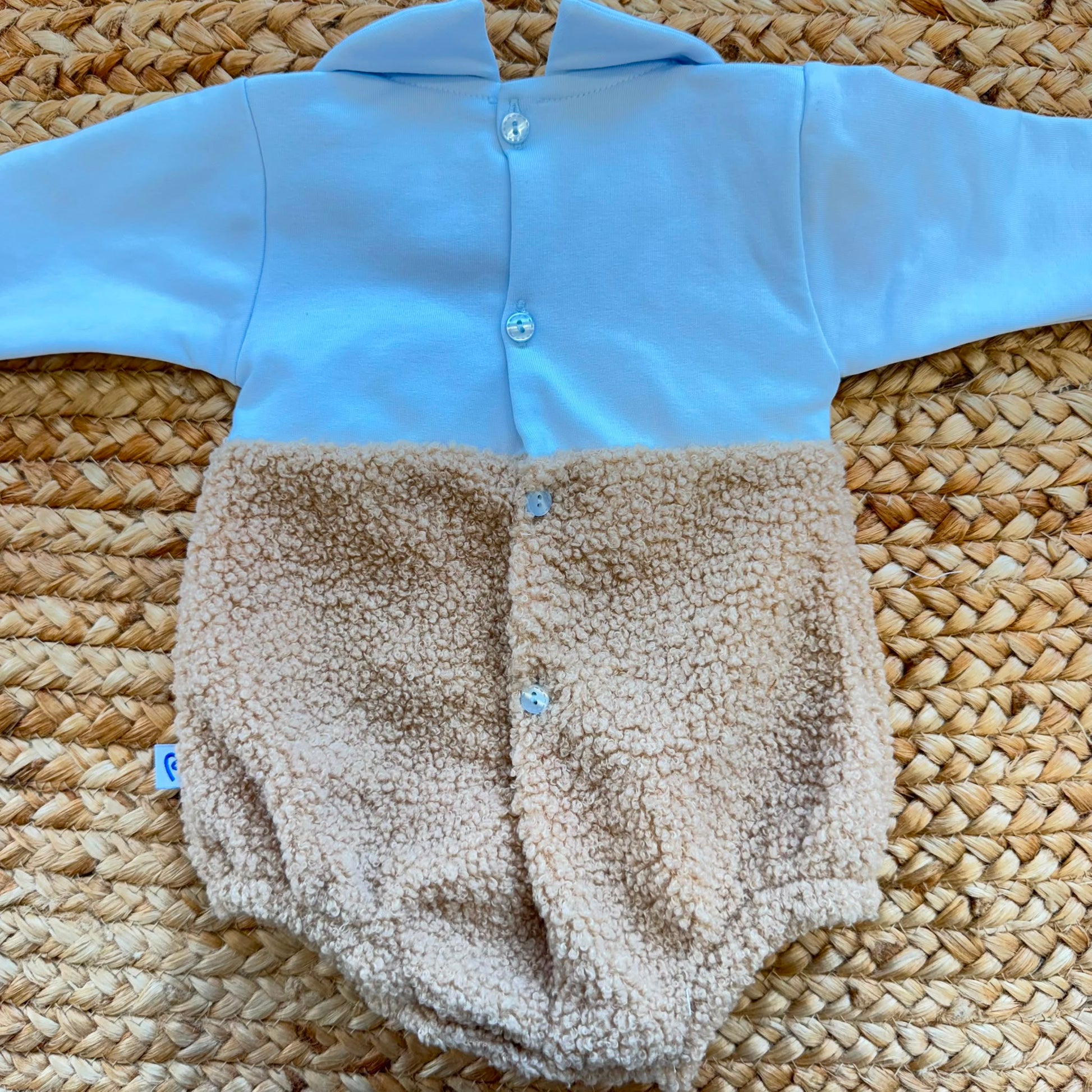 Dettaglio del tessuto teddy e dei bottoni del pagliaccetto neonato azzurro in caldo cotone.