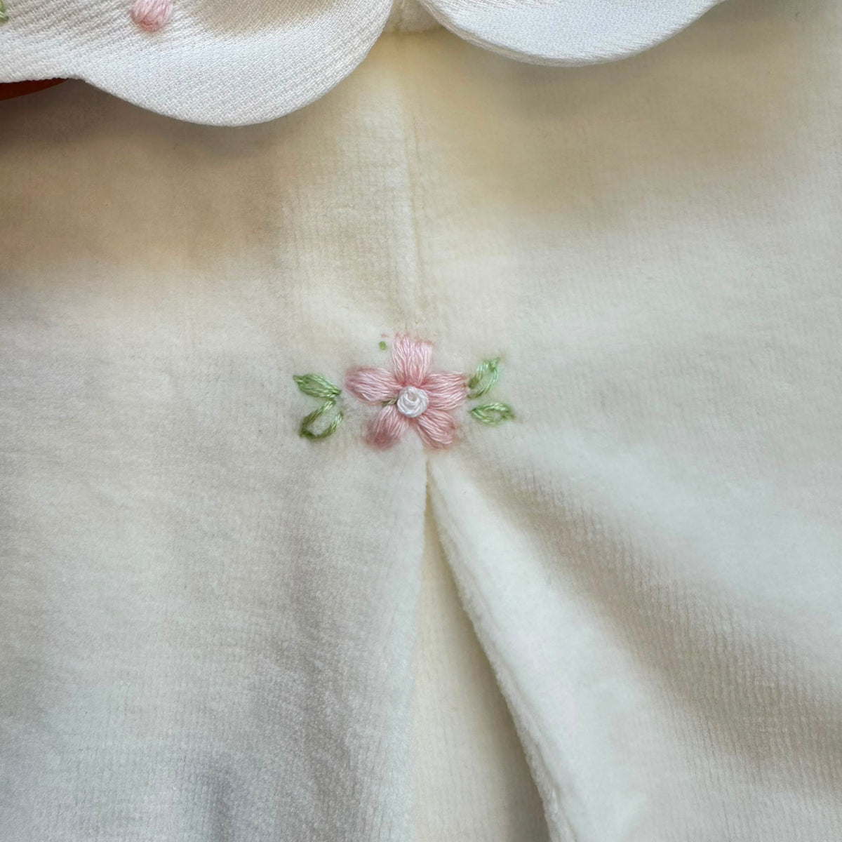 Tutina in ciniglia neonata colore latte con colletto ricamato a fiori rosa e ricamo floreale sul davanti.