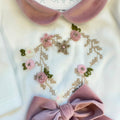Uscita clinica neonata in ciniglia bianca e rosa con completino ricamato a cuore floreale, fiocco applicato, cappello, bavetta, scarpine, lenzuola coordinate e copertina sfoderabile.