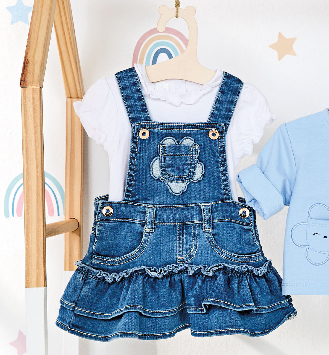 Salopette neonata in denim con fiore ricamato e balze, indossata con body bianco