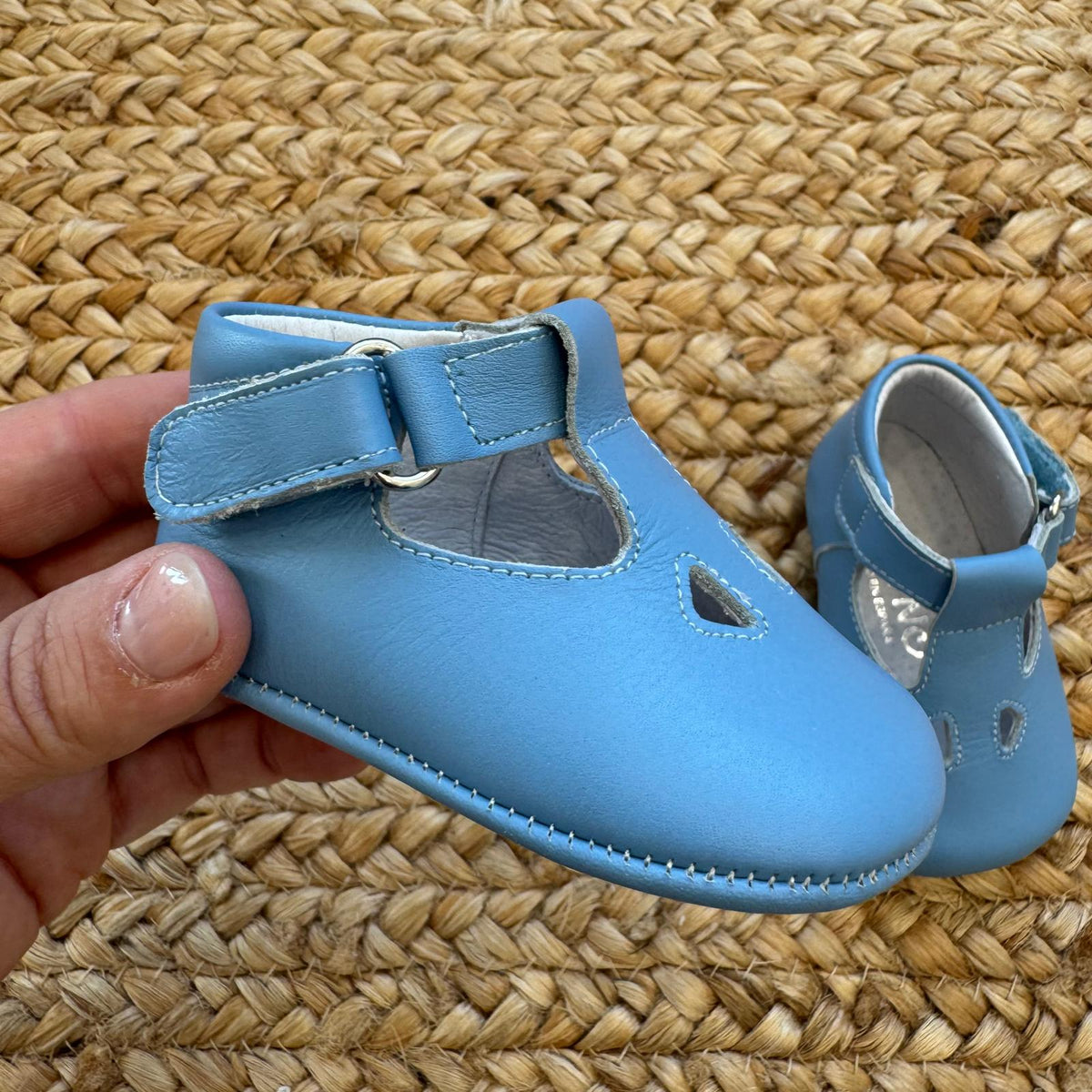 Scarpe battesimo bimbo azzurro con cinturino e dettagli decorativi frontali.