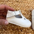 Scarpe battesimo bimbo bianche con cinturino e dettagli frontali decorativi.