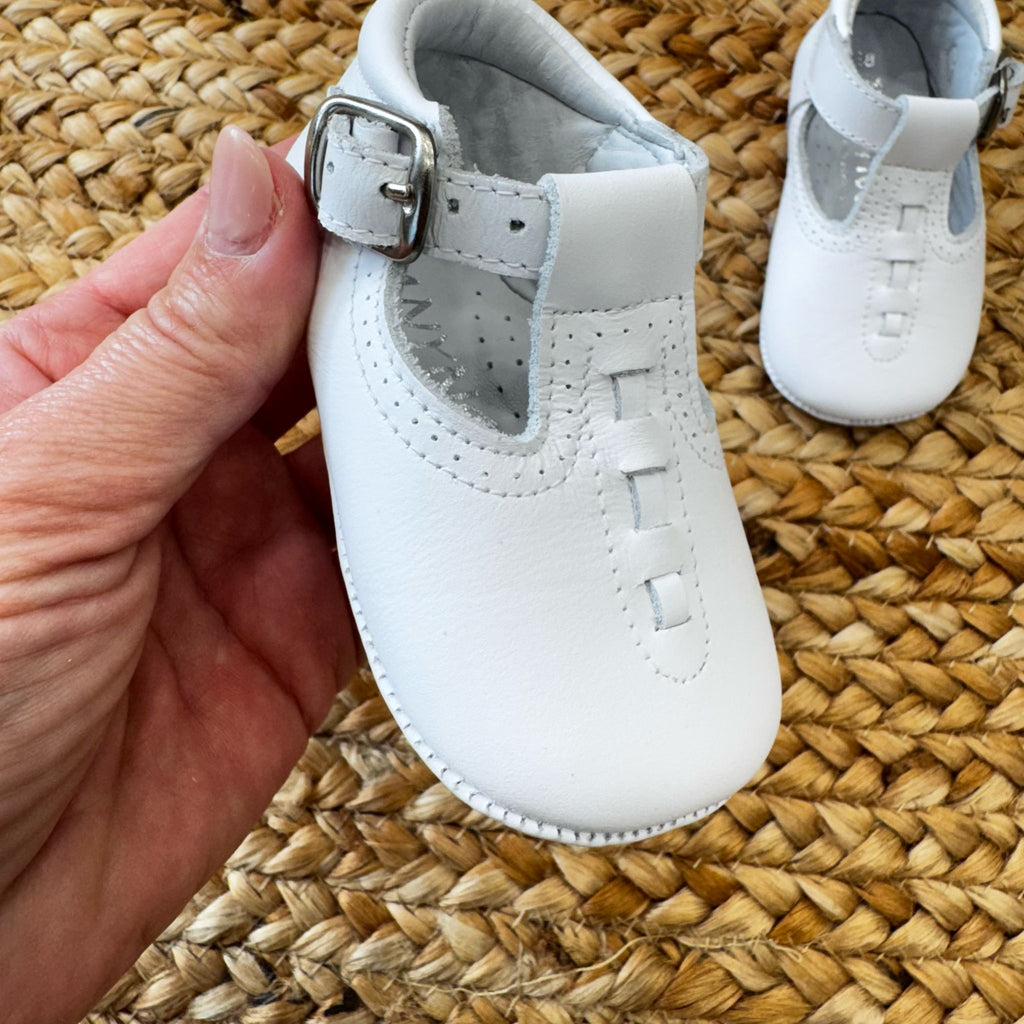 Scarpa culla in pelle bianca con cinturino regolabile.