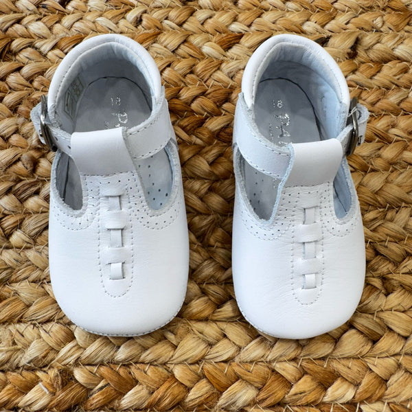 Scarpa culla in pelle bianca con cinturino regolabile.