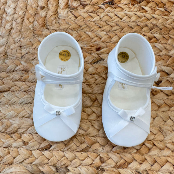 Scarpa culla in raso avorio con fiocco e strass, vista dall’alto.