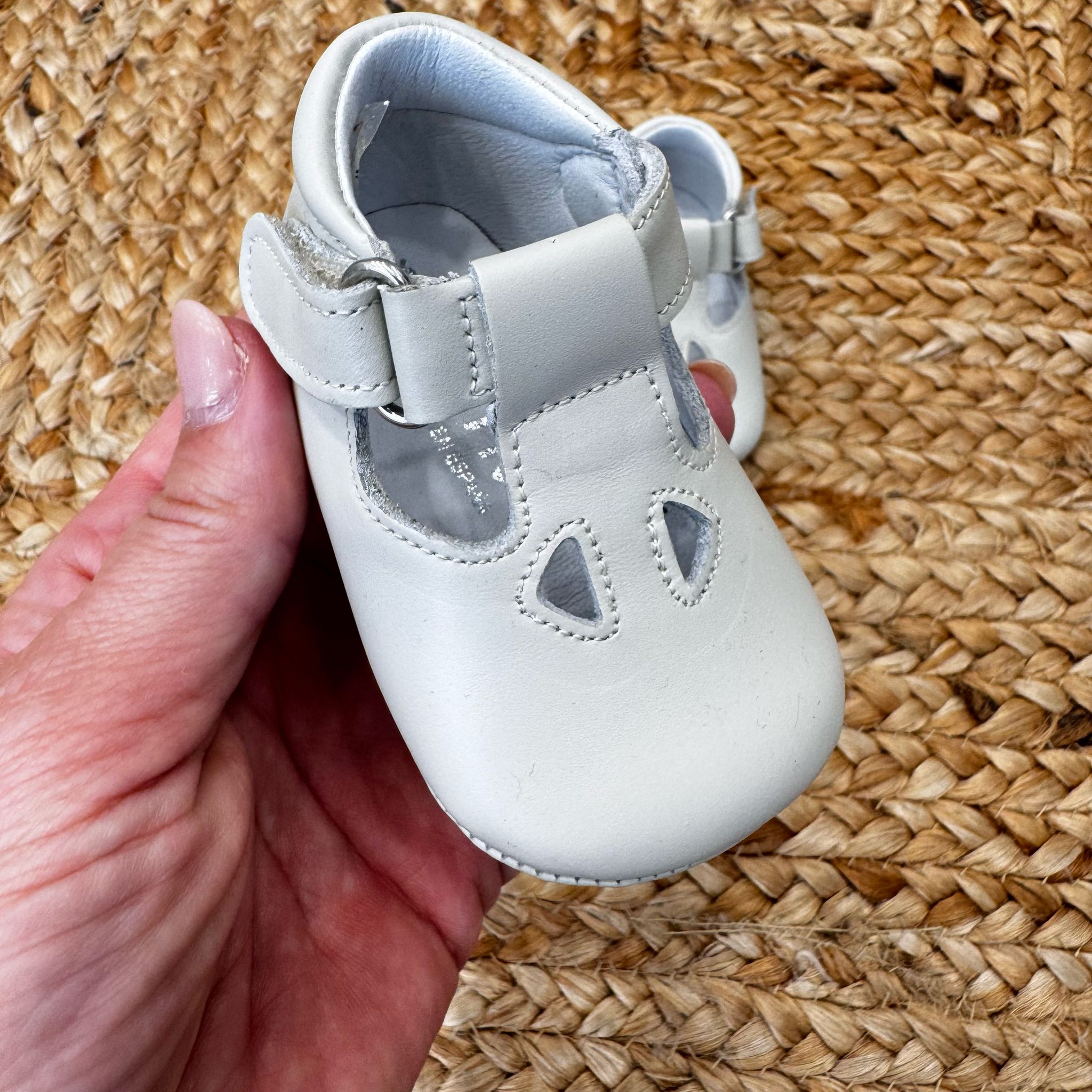 Scarpa culla in pelle bianca con cinturino regolabile e fori decorativi