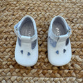 Scarpe battesimo bimbo bianche con cinturino e dettagli frontali decorativi.
