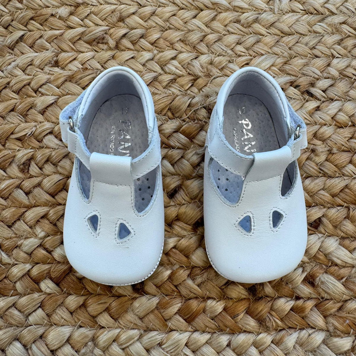 Scarpe battesimo bimbo bianche con cinturino e dettagli frontali decorativi.