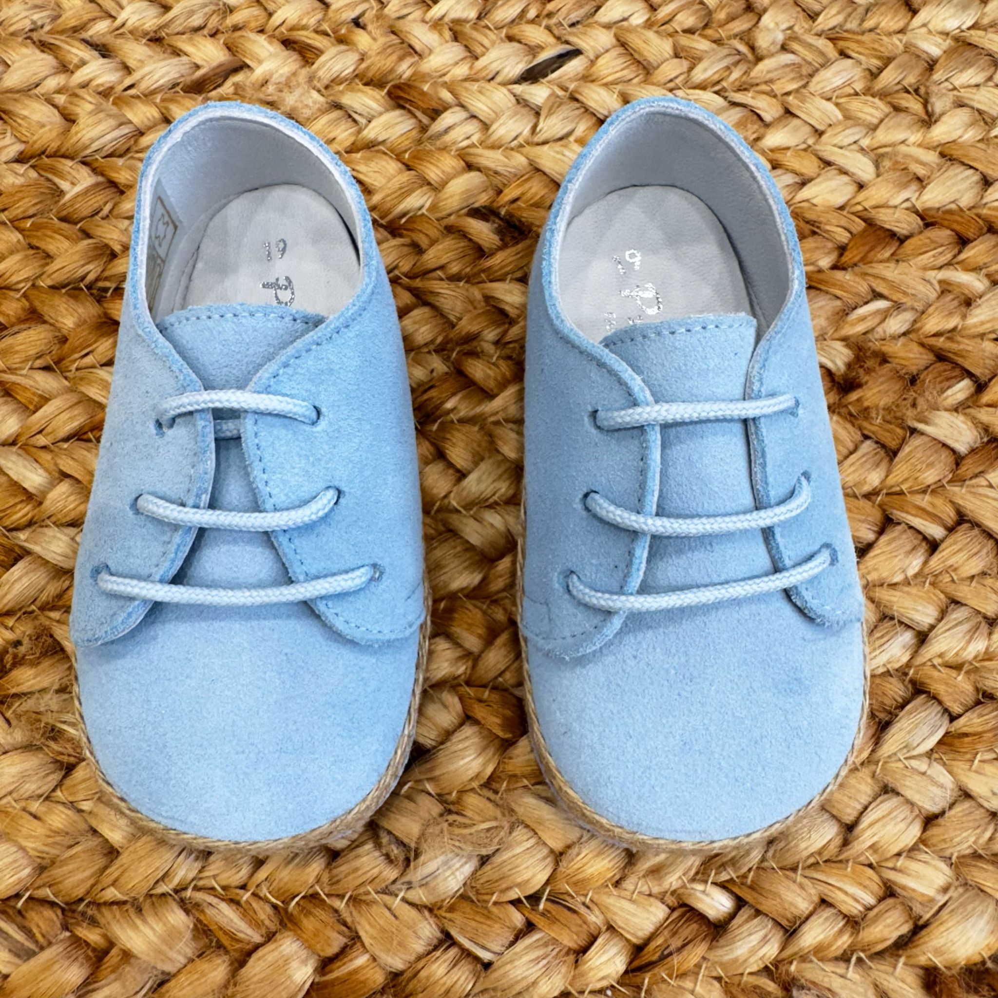 Scarpe culla azzurre in camoscio con lacci e bordo intrecciato effetto corda, ideali per neonati in occasioni speciali.

