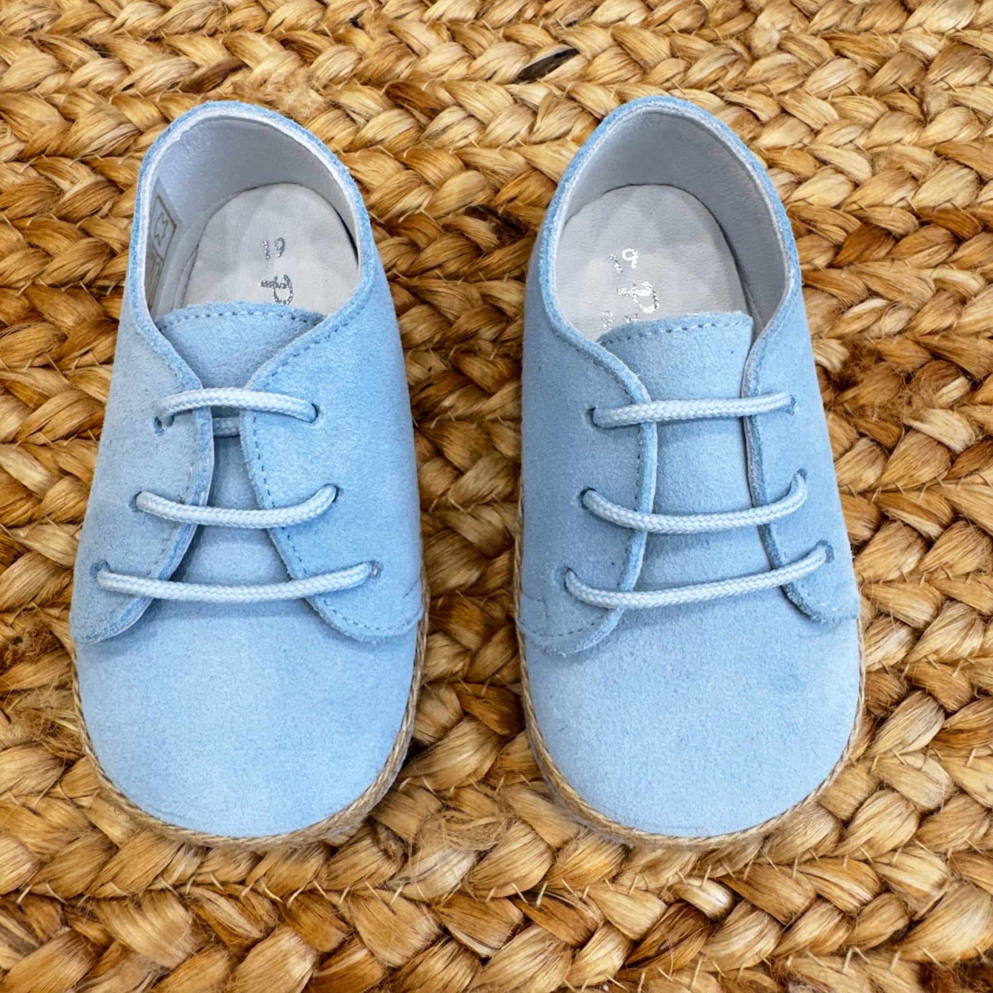 Scarpe culla azzurre in camoscio con lacci e bordo intrecciato effetto corda, ideali per neonati in occasioni speciali.

