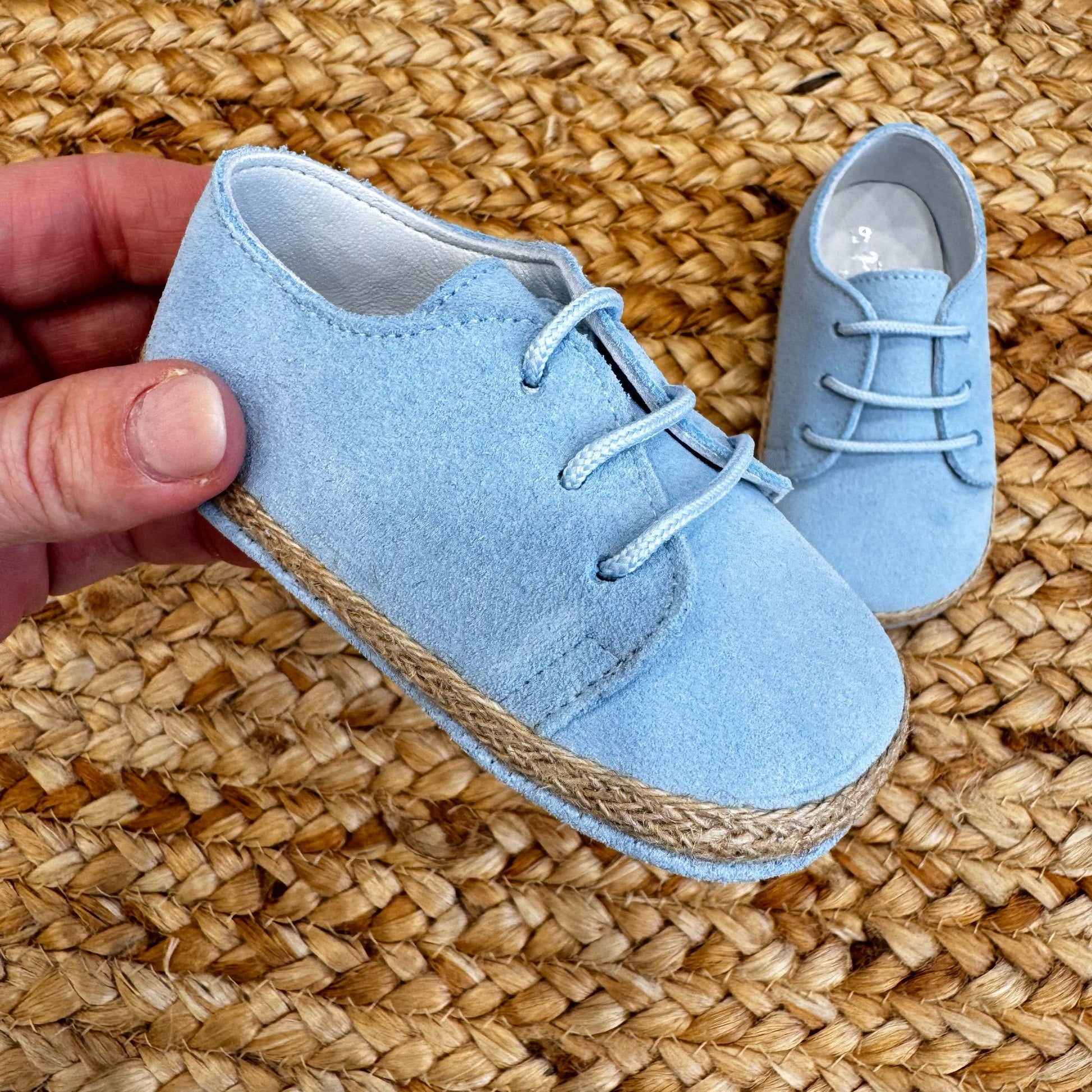 Scarpe culla azzurre in camoscio con lacci e bordo intrecciato effetto corda, ideali per neonati in occasioni speciali.

