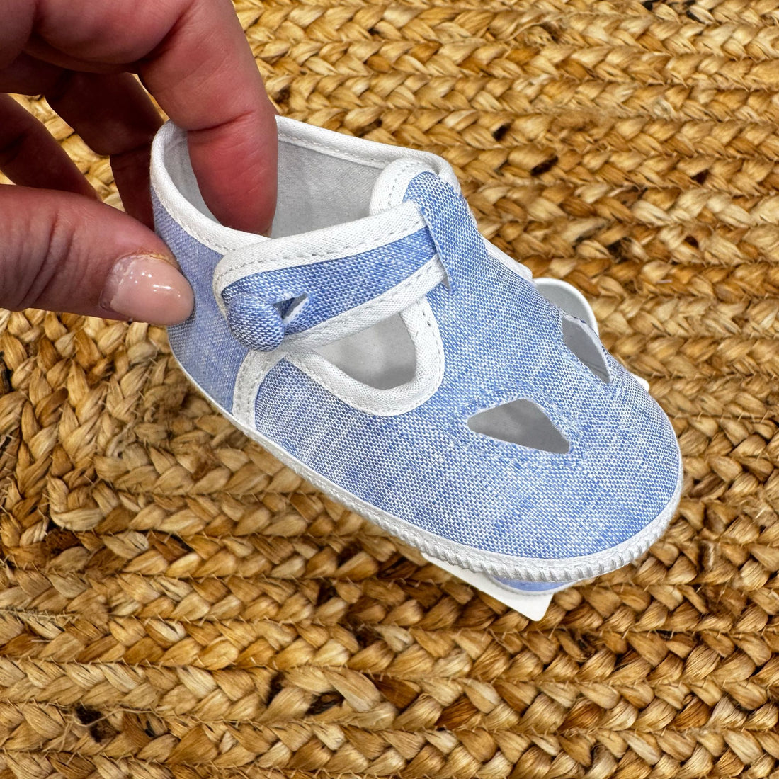 Scarpe culla in tessuto azzurro con dettagli traforati e chiusura con cinturino regolabile, ideali per neonati in primavera ed estate.