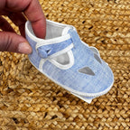 Scarpe culla in tessuto azzurro con dettagli traforati e chiusura con cinturino regolabile, ideali per neonati in primavera ed estate.
