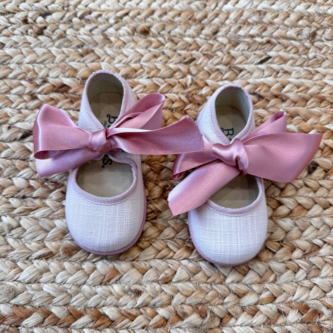Scarpe culla modello ballerina in tessuto rosa con fiocco in raso coordinato, ideali per cerimonie e occasioni speciali.