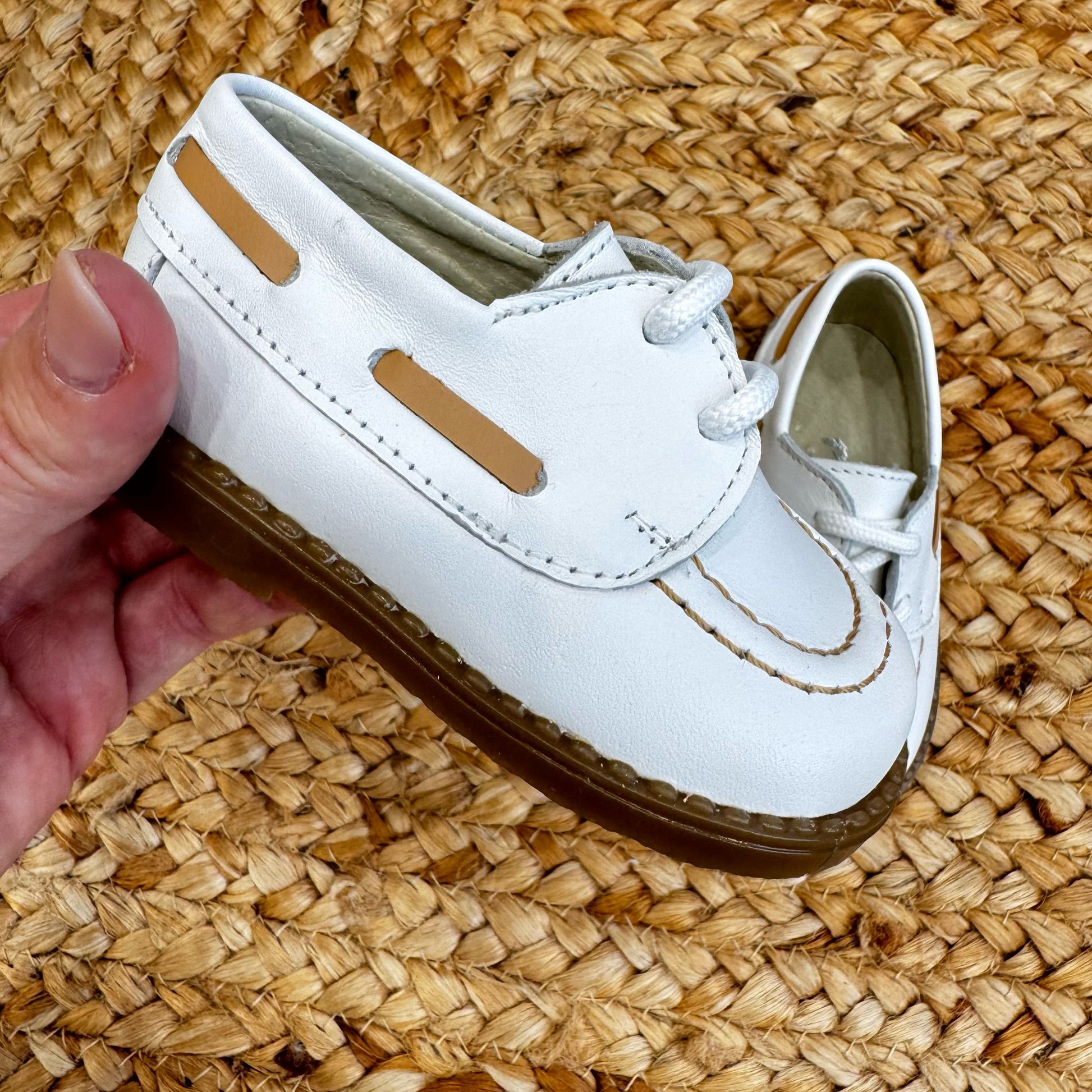 Scarpe culla modello barchetta in pelle bianca con cuciture a contrasto e chiusura a lacci, ideali per neonati in occasioni speciali.


