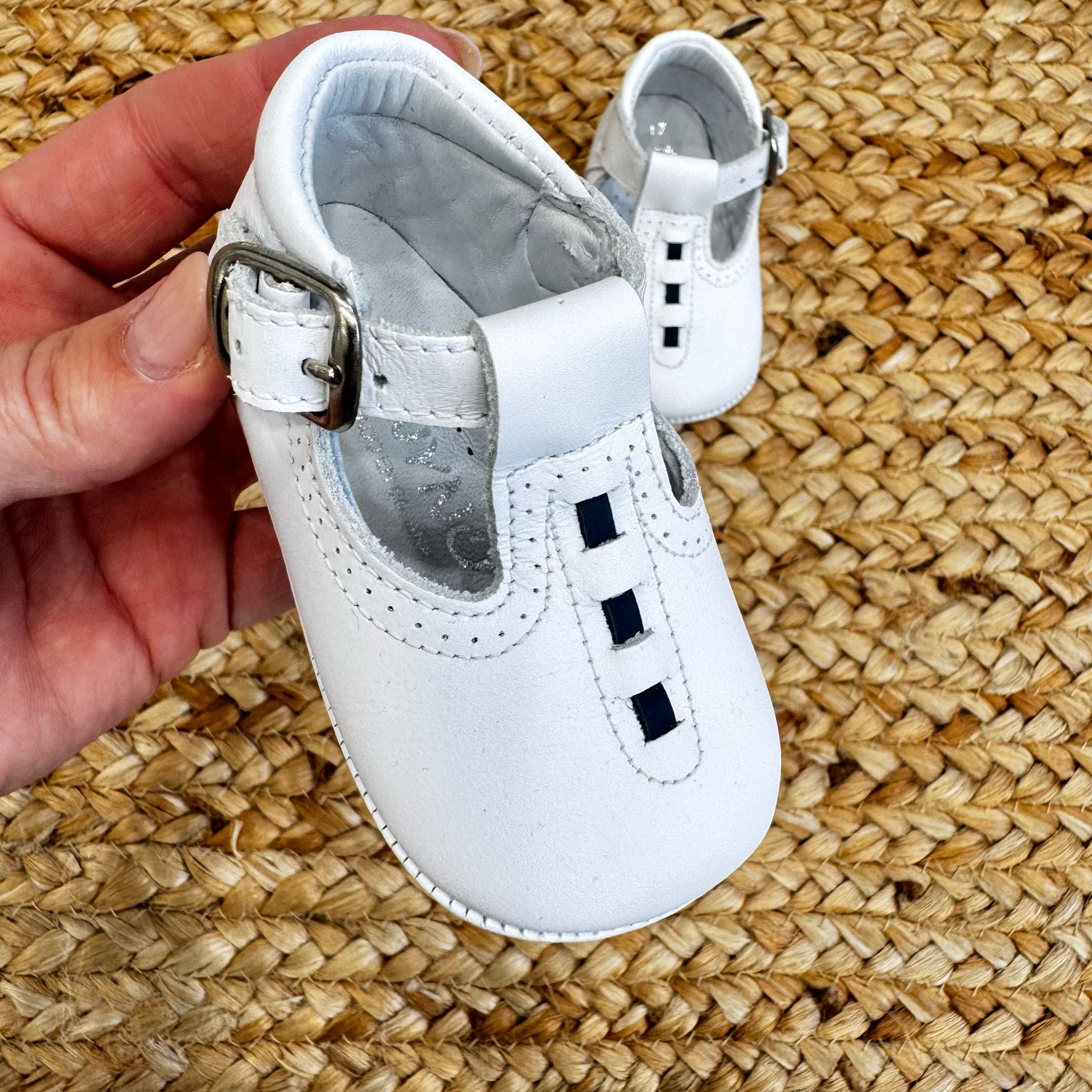 Scarpe culla bianche in pelle con design T-bar e chiusura laterale con fibbia, ideali per battesimo e cerimonia.