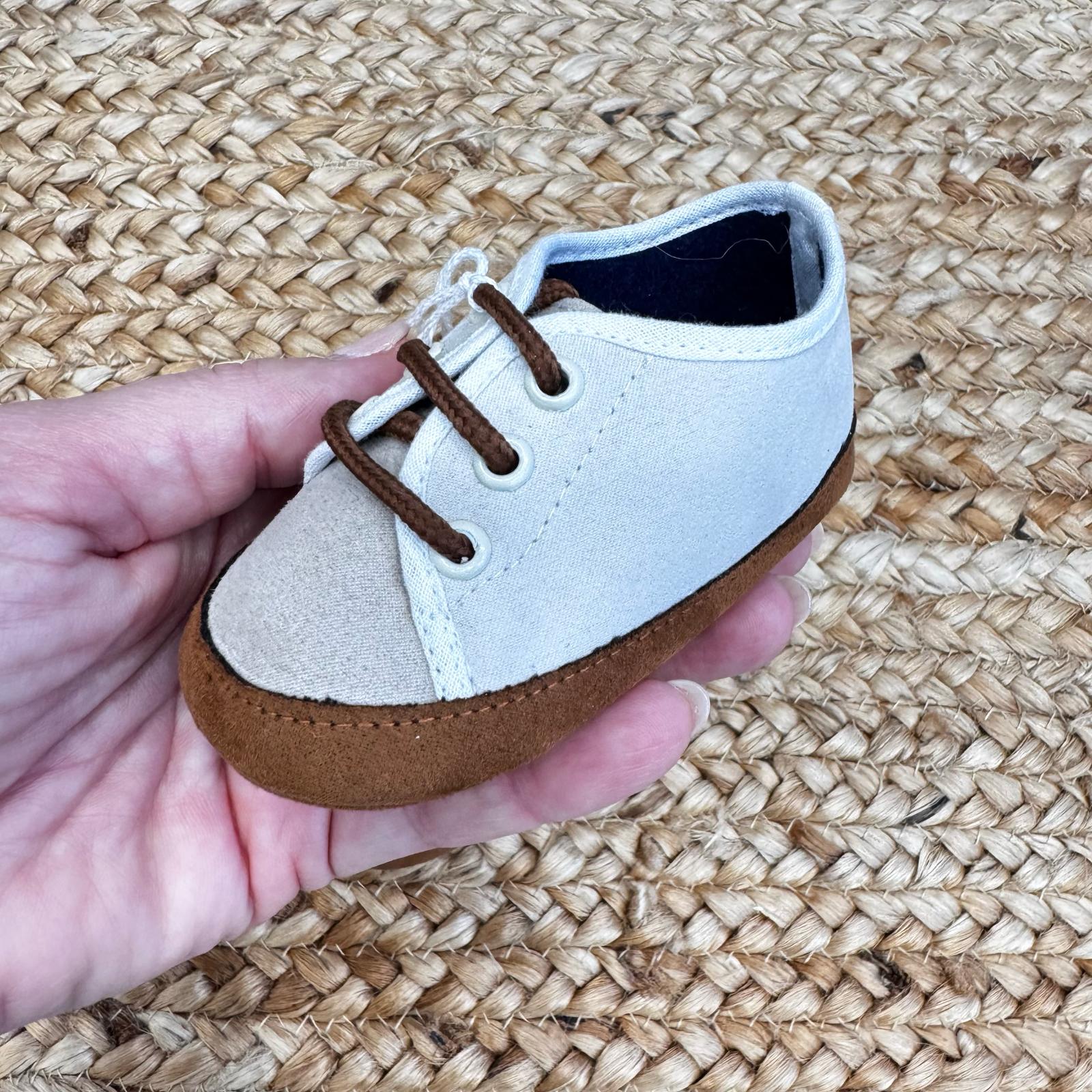 Scarpe culla in tessuto bicolore beige e bianco con punta rinforzata in suede marrone e chiusura a lacci. Perfette per neonati.