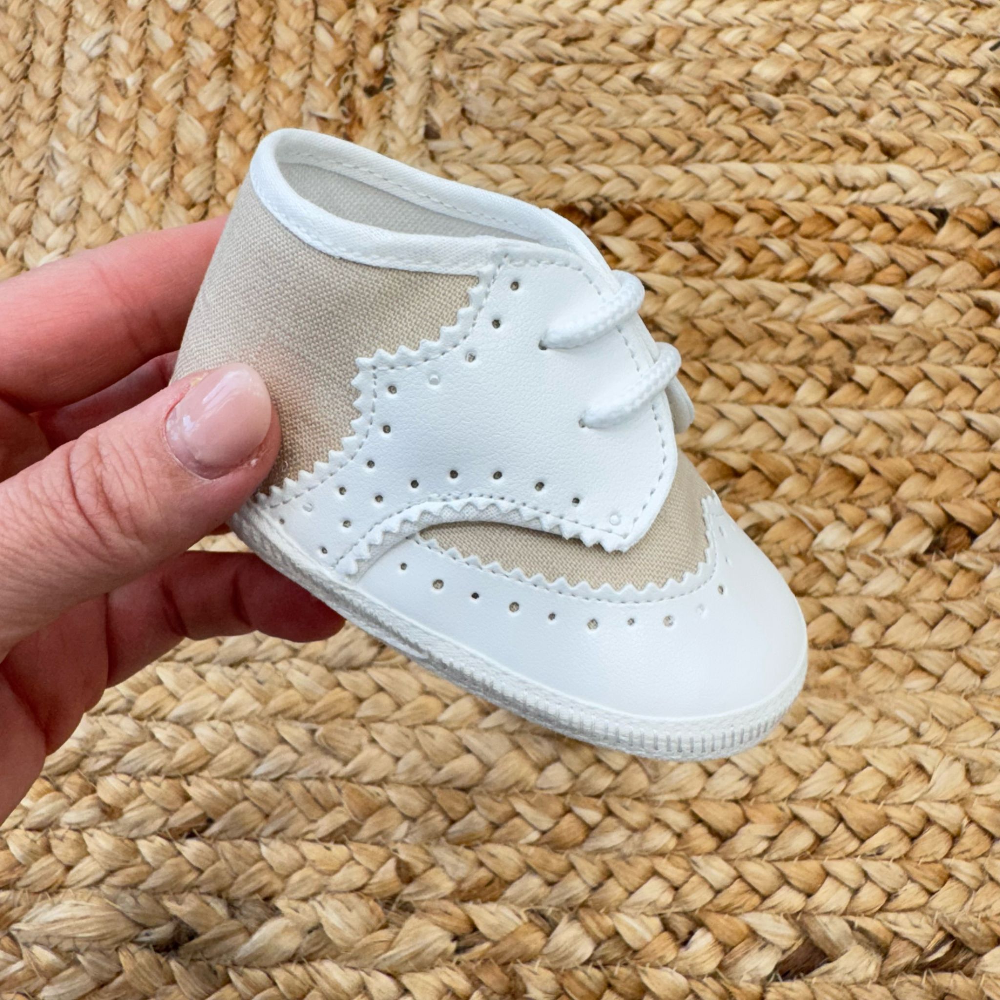 Scarpe culla in stile brogue con dettagli traforati, in bianco e beige, con chiusura a lacci. Ideali per battesimo e cerimonia.