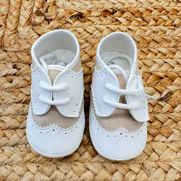 Scarpe culla in stile brogue con dettagli traforati, in bianco e beige, con chiusura a lacci. Ideali per battesimo e cerimonia.
