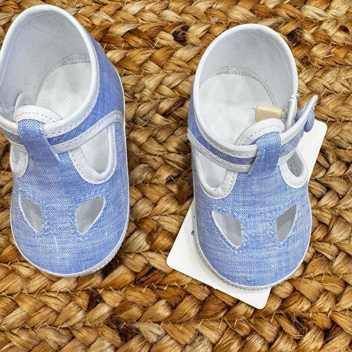 Scarpe culla in tessuto azzurro con dettagli traforati e chiusura con cinturino regolabile, ideali per neonati in primavera ed estate.