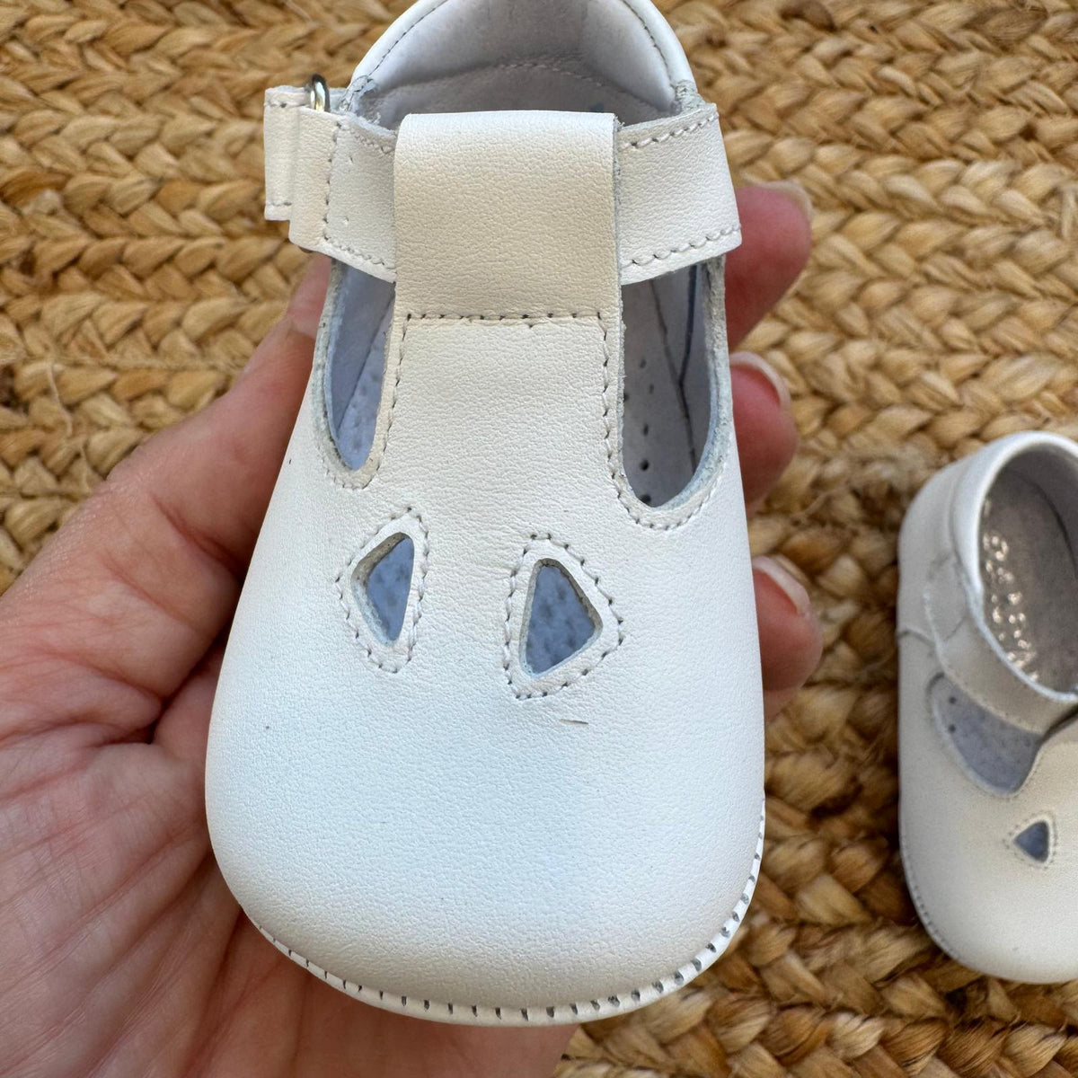 Scarpe battesimo bimbo bianche con cinturino e dettagli frontali decorativi.