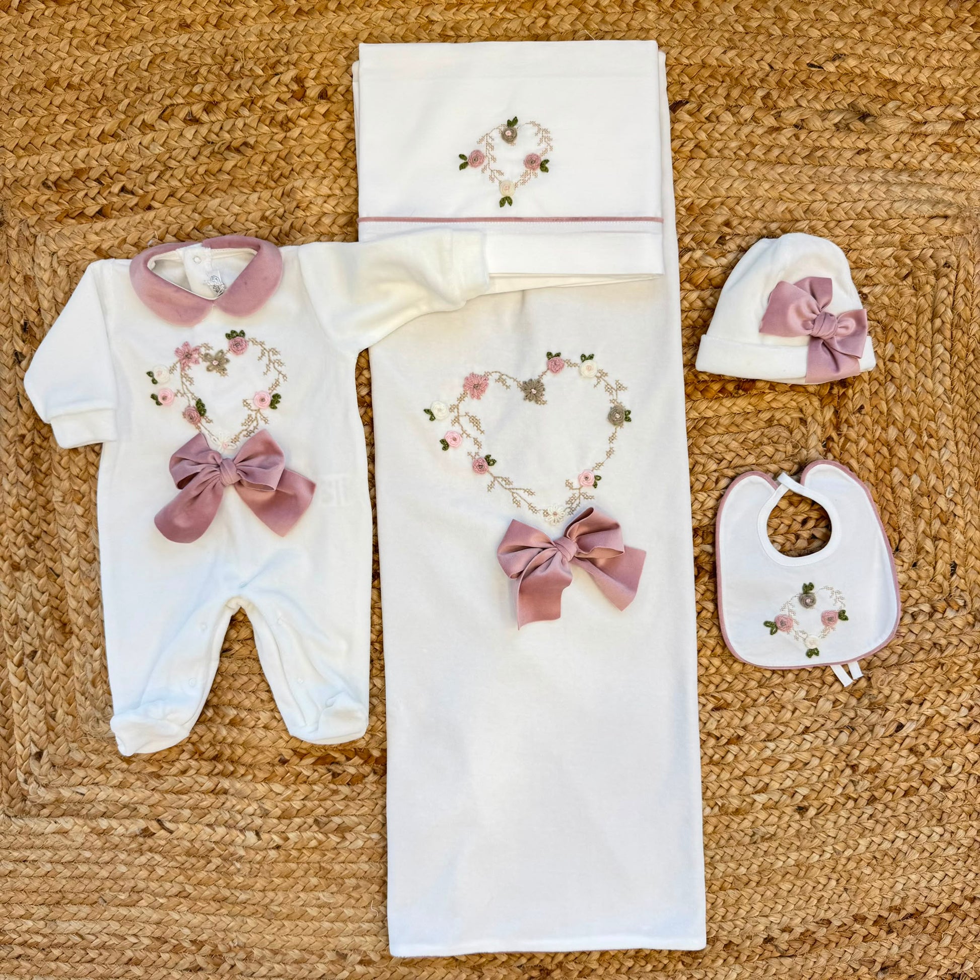 Uscita clinica neonata in ciniglia panna con ricamo floreale a cuore e fiocco rosa composta da tutina, bavetta, cappellino, lenzuola coordinate e copertina sfoderabile.