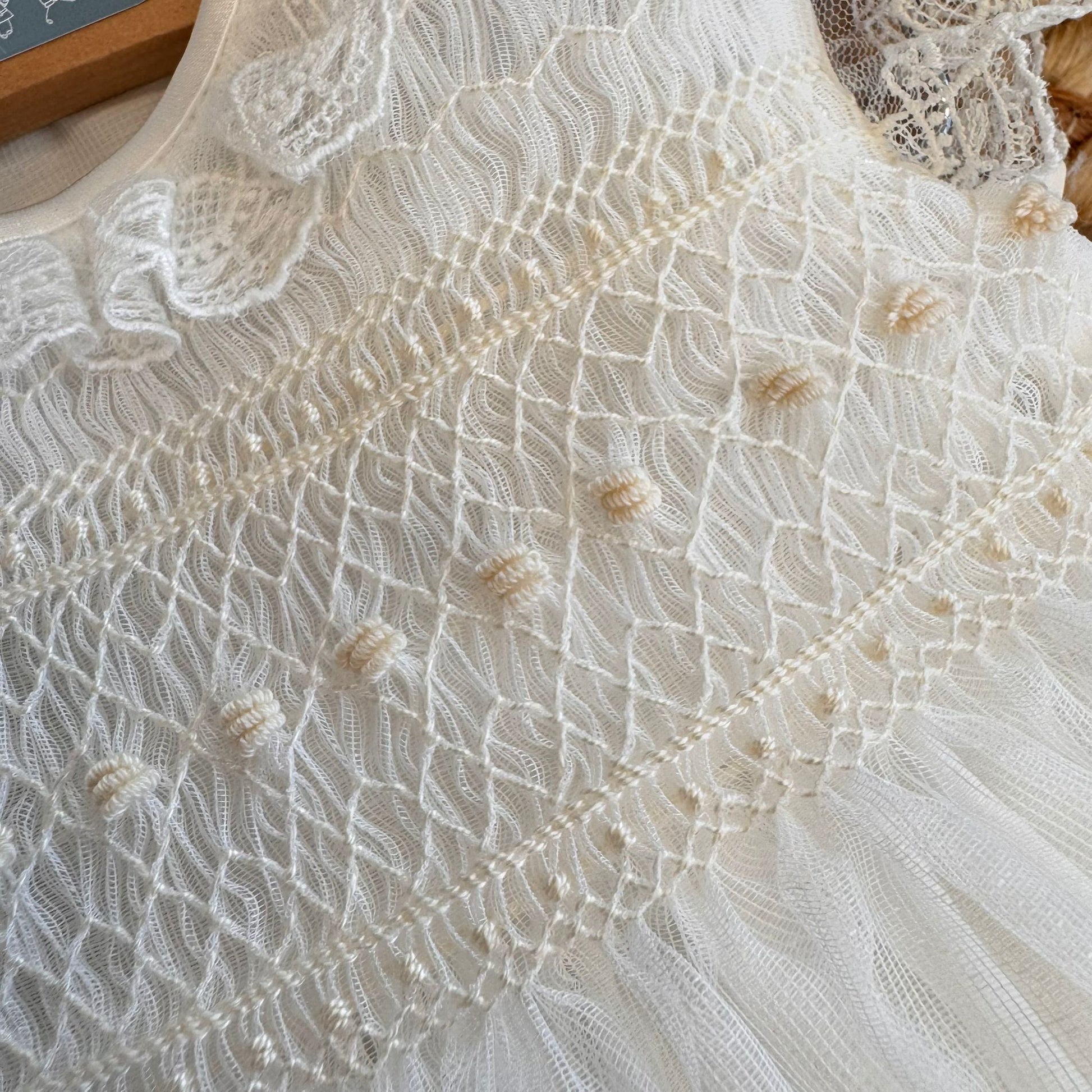 Lavorazione smock ricamata a mano in beige chiaro su abito da Battesimo