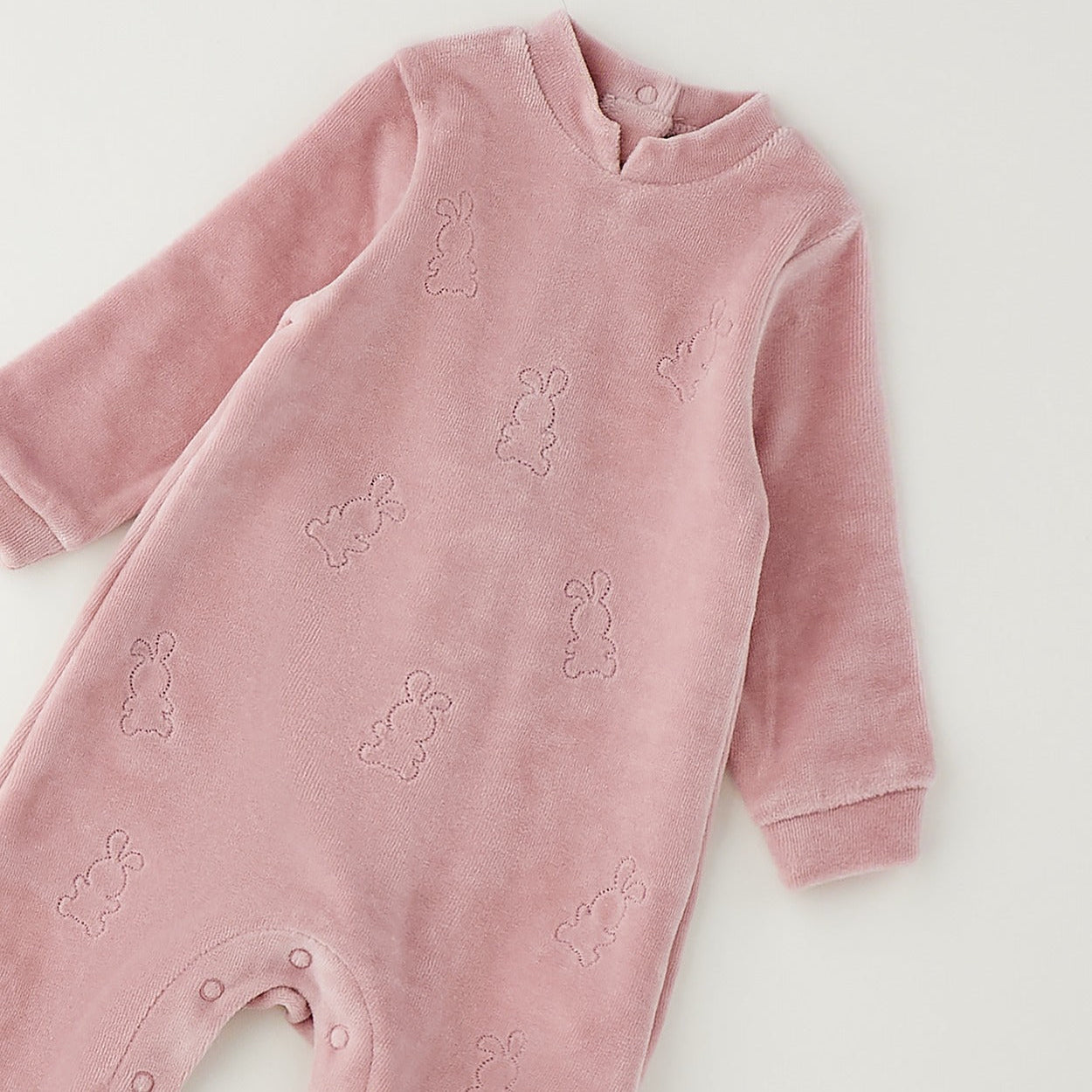 Retro tutina neonata in ciniglia rosa con chiusura a bottoncini e dettaglio a quadretti sui piedini.